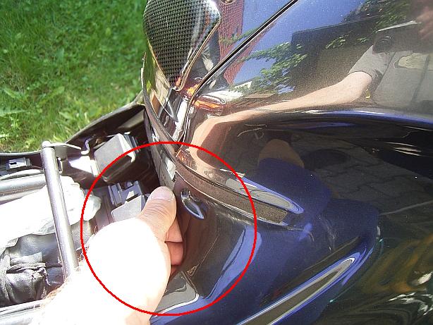 Mit der zweiten Hand packst du die Verkleidung hier und ziehst sie vorsichtig am Tankbereich nach oben, bis die Verkleidung sich an der Tankverkleidung ausklinkt.